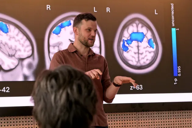 Man presenterar forskning. Bilder på hjärnor i bakgrunden.